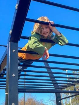 Boy climbing high on playground structure against clear blue sky Stock Photos