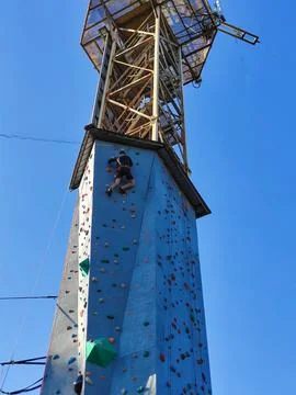 A boy climbs a high tower with walls for climbing on hooks in special equipment Foto stock