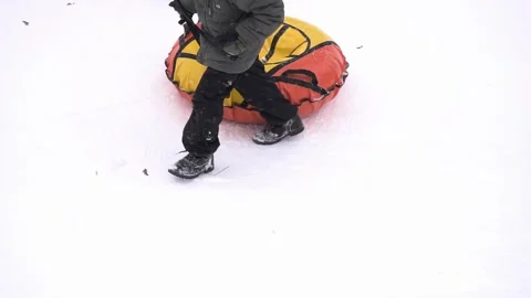 A boy climbs a hill and pulls a tubing tube behind him, slow motion Stock Footage 314427839