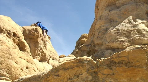 Boy climbs rock formation while man approaches. Video stock 29592259