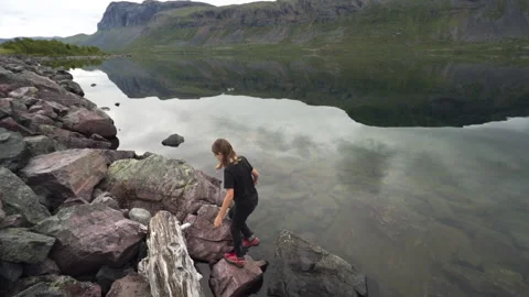 Boy climbs on rocks next to mirrored lake in Swedish Lapland with insects Stock Footage 147839833