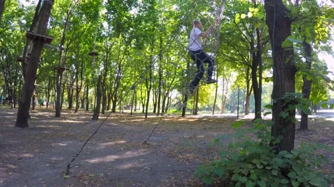 The boy climbs up a tree to the grid. Children playing in the park 库存影片 54743253
