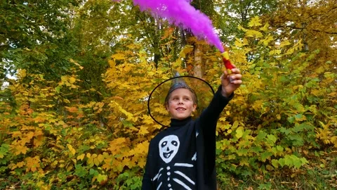 A boy with colored smoke in his hands in a skeleton costume, wearing a hat Stock Footage 204084789