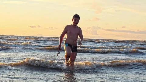 A boy comes ashore from the ocean after swimming with swimming goggles in his 스톡 사진