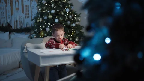 Boy Composes Letter Santa at Table, Happy Expectation in Festively Adorned Home Stock Footage 258102578