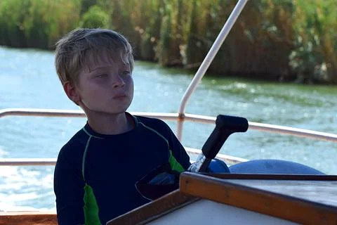 A boy with a concentrated look drives a large motor boat. 스톡 사진
