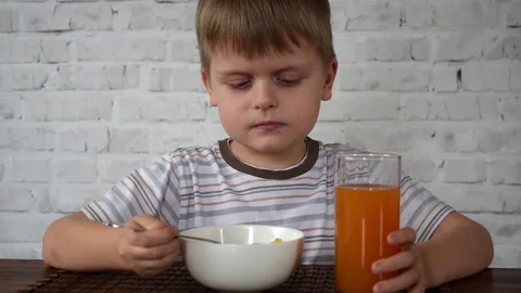 Boy with corn flakes and juice eating at the wooden table Stock Footage 72955053
