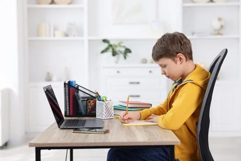 Boy with correct posture doing homework at wooden desk indoors Stock Photos
