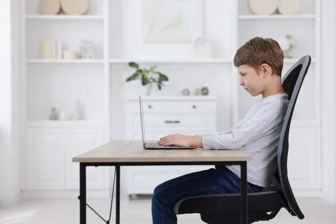 Boy with correct posture using laptop at wooden desk indoors Stock Photos