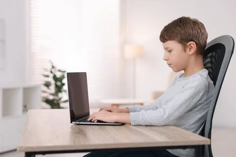 Boy with correct posture using laptop at wooden desk indoors Stock Photos