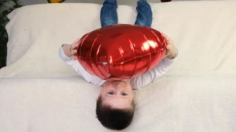 Boy on the couch is playing  with a red heart-shaped ball Stock Footage 146164183
