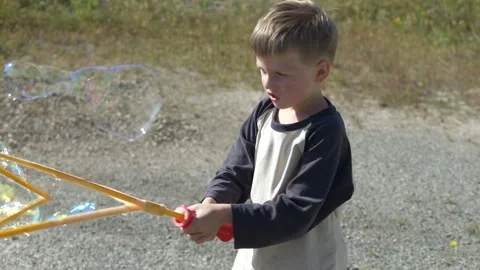 Boy creating large soap bubbles in outdoor setting with toy, child activity Video stock 333773451