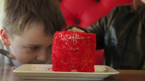 The boy is cut into a cake on a plate. Red sponge cake in focus, boy out of Stock Footage 154209117