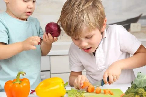 The boy cut the carrots on the kitchen table. Stock Photos