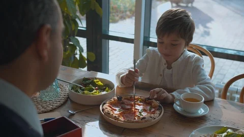Boy cuts pizza with a knife, father helps him Stock Footage 120734801