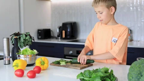 A boy is cutting a cucumber at the table. The child is preparing a salad Stock Footage 261476812