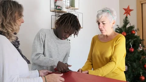 Boy cutting wrapped paper while wrapping christmas presents with his mothers at Stock Footage 246545055