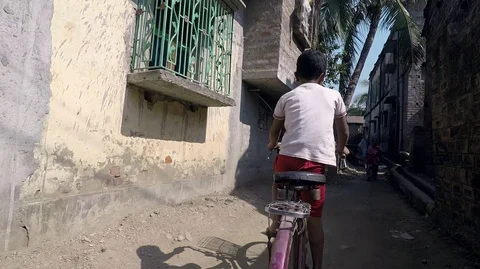 Boy cycles and pushes his bike through village alley Stock Footage 87440926