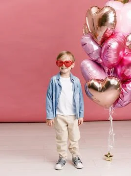 Boy dancing, smiling and having fun near  big branch of pink heart-shaped bal Stock Photos