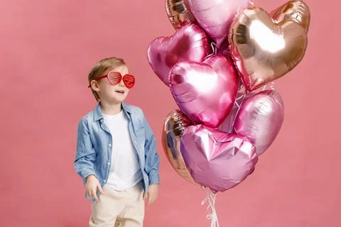Boy dancing, smiling and having fun near  big branch of pink heart-shaped bal Stock Photos