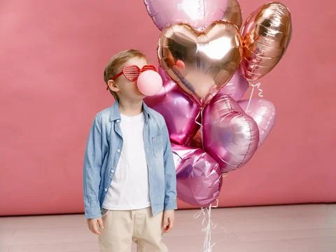 Boy dancing, smiling and having fun near  big branch of pink heart-shaped bal Stock Photos