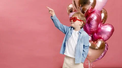 Boy dancing, smiling and having fun near  big branch of pink heart-shaped bal Stock Photos