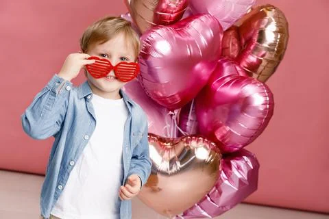 Boy dancing, smiling and having fun near  big branch of pink heart-shaped bal Stock Photos