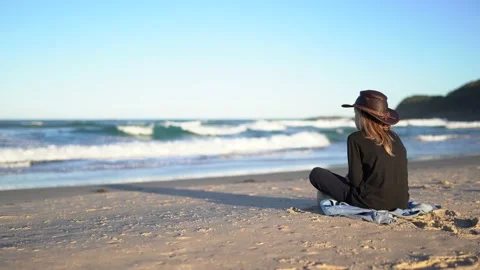 A boy in dark clothes sits on a sand beach looking at ocean waves. Stock Footage 140952227