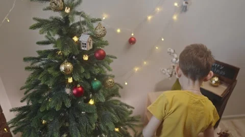 Boy decorates a Christmas tree by hanging Christmas toy balls in the room Video stock 291605059