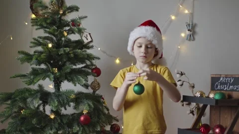 Boy decorates a Christmas tree by hanging Christmas toy balls in the room Video stock 291605344