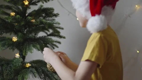 Boy decorates a Christmas tree by hanging Christmas toy balls in the room Video stock 291605500