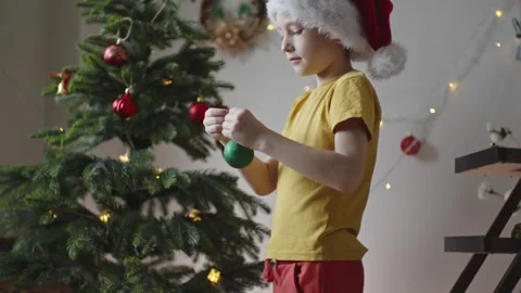 Boy decorates a Christmas tree by hanging Christmas toy balls in the room Video stock 291605599