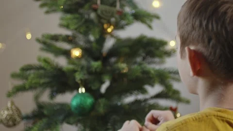 Boy decorates a Christmas tree by hanging Christmas toy balls in the room Video stock 291605668