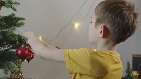 Boy decorates a Christmas tree by hanging Christmas toy balls in the room Video stock 291605996