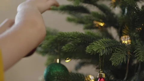 Boy decorates a Christmas tree by hanging Christmas toy balls in the room Video stock 291606160