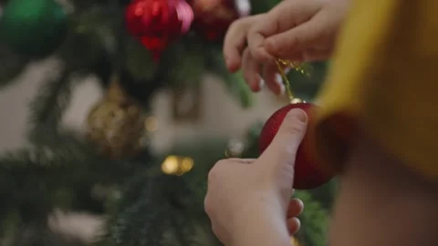 Boy decorates a Christmas tree by hanging Christmas toy balls in the room Video stock 291606264