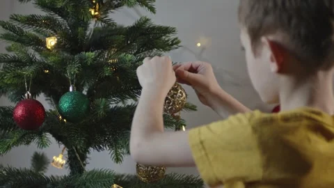 Boy decorates a Christmas tree by hanging Christmas toy balls in the room Video stock 291606326
