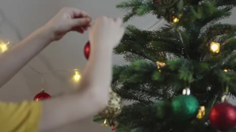 Boy decorates a Christmas tree by hanging Christmas toy balls in the room Video stock 291606498
