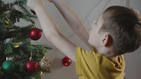 Boy decorates a Christmas tree by hanging Christmas toy balls in the room Video stock 291606568