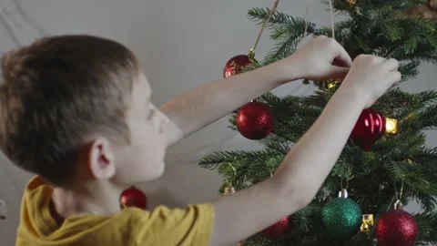 Boy decorates a Christmas tree by hanging Christmas toy balls in the room Video stock 291606654