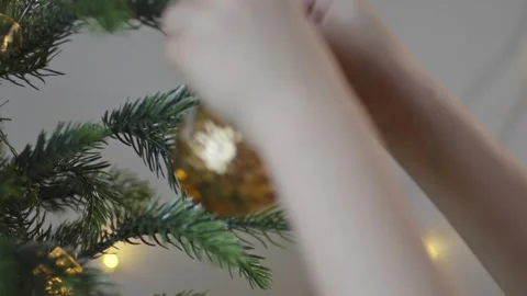 Boy decorates a Christmas tree by hanging Christmas toy balls in the room Video stock 291606700