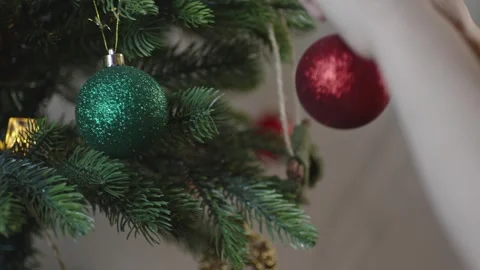 Boy decorates a Christmas tree by hanging Christmas toy balls in the room Video stock 291606921
