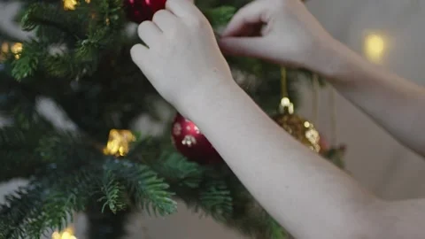 Boy decorates a Christmas tree by hanging Christmas toy balls in the room Stock Footage 291607182