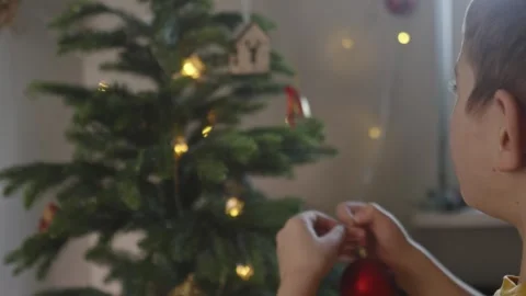 Boy decorates a Christmas tree by hanging Christmas toy balls in the room Video stock 291607304