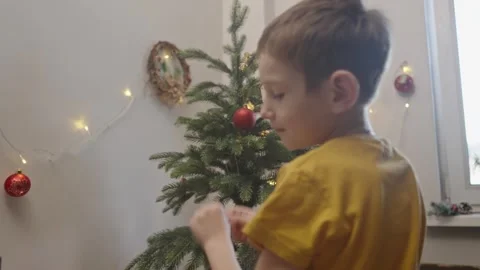 Boy decorates a Christmas tree by hanging Christmas toy balls in the room Stock Footage 291607587