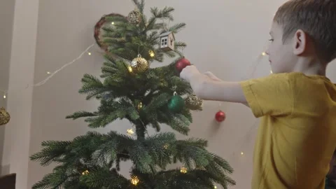 Boy decorates a Christmas tree by hanging Christmas toy balls in the room Stock Footage 291607868