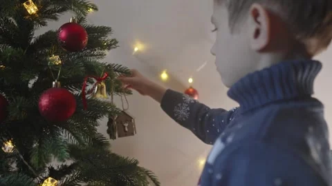 Boy decorates a Christmas tree by hanging Christmas toy balls in the room Stock Footage 291608410