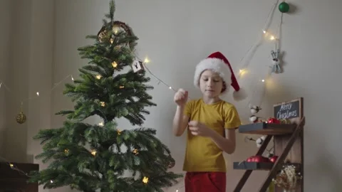 Boy decorates a Christmas tree by hanging Christmas toy balls in the room Stock Footage 291608770
