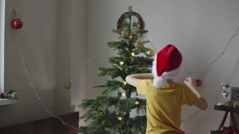 Boy decorates a Christmas tree by hanging Christmas toy balls in the room Stock Footage 291608772