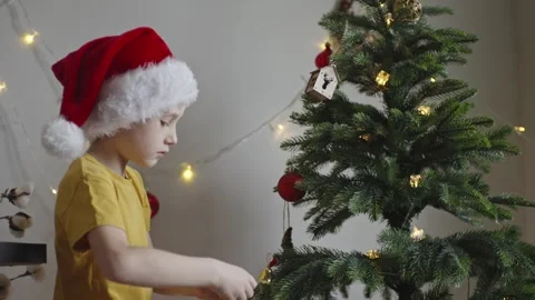 Boy decorates a Christmas tree by hanging Christmas toy balls in the room Stock Footage 291608995
